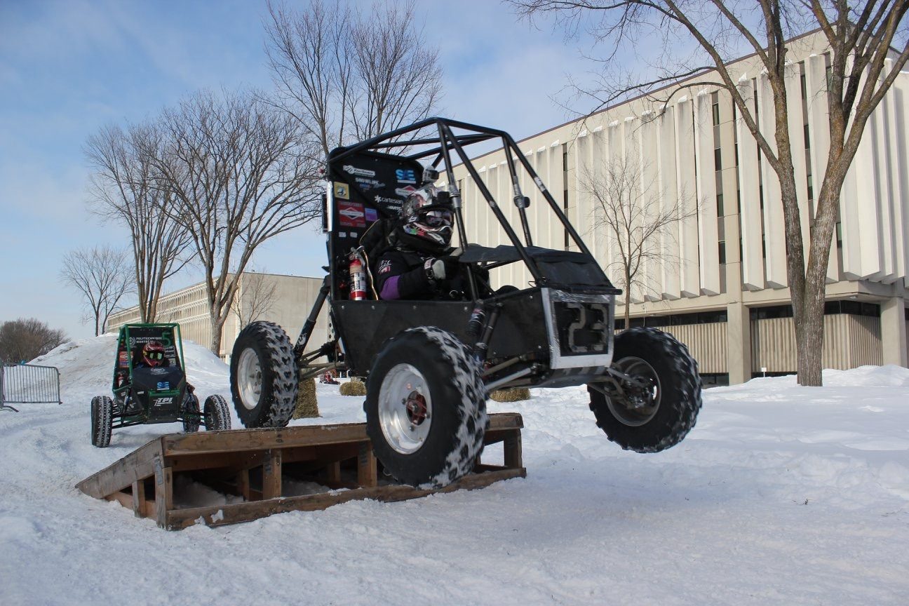 Baja SAE car clearing a wooden ramp at the winter competition with a second car behind